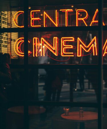 un uomo scatta una foto ad una vetrina dove si riflette la scritta in neon arancione "Central Cinema".