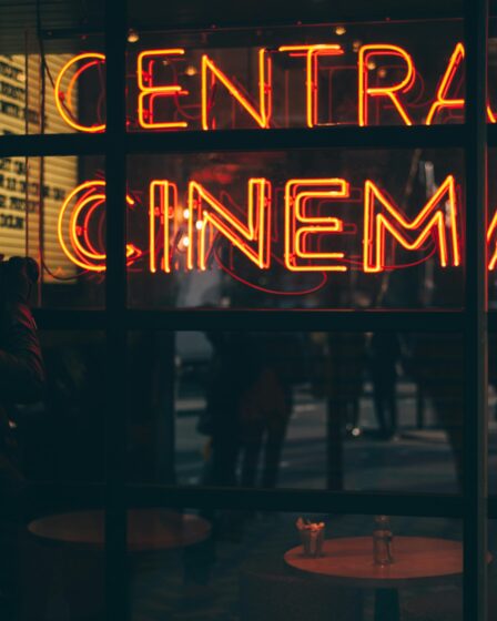 un uomo scatta una foto ad una vetrina dove si riflette la scritta in neon arancione "Central Cinema".